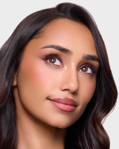 Woman with long, wavy hair against a plain background wearing Dimple Color's Serenity Brown color contact lenses